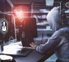 Hacker mit grauem Kapuzenpullover sitzt vor Bilderschirmen